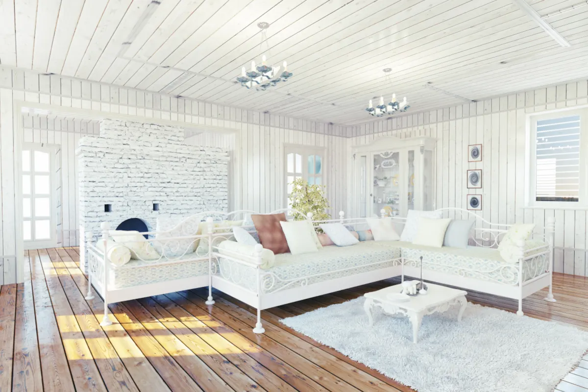 Salon w stylu prowansalskim. Duże kanapy z metalową konstrukcją w kolorze białym. Ściany oraz sufit stanowią deski drewniane pomalowane na biało.