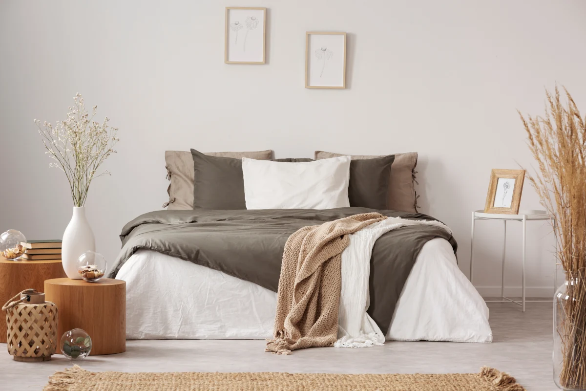 Łóżko w sypialni z poduszkami oraz narzutami w kolorze ziemi. Obok łóżka dekoracje w stylu skandynawskim.
