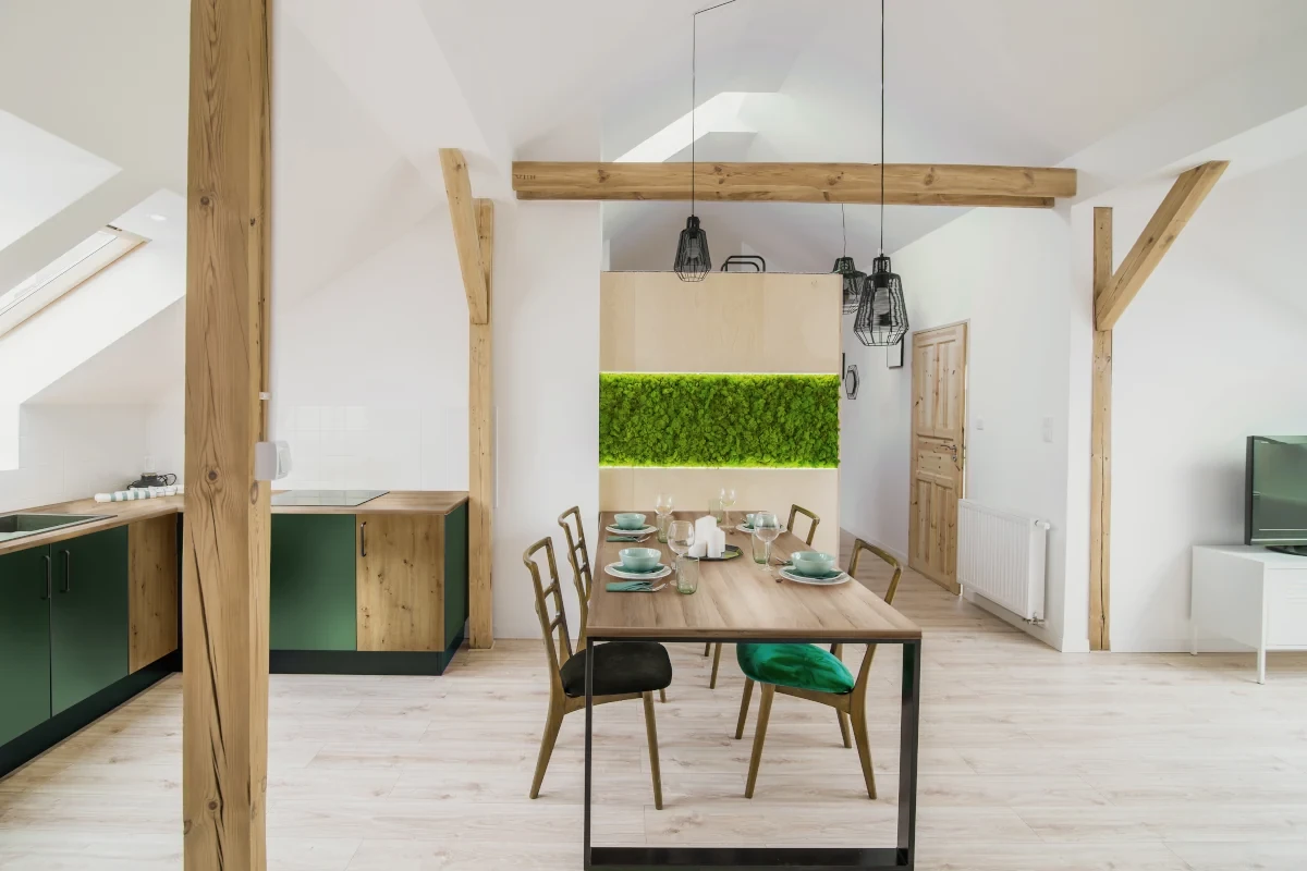 Kuchnia styl Vintage na poddaszu. Meble połączenie drewna oraz koloru zielonego. Blat kuchenny dąb lorenzo.  Stół stojący na środku pomieszczenia z krzesłami z zielonymi siedziskami.