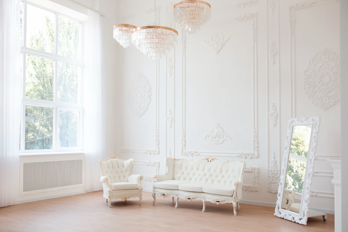 Biała sofa oraz fotel ze złotymi akcentami na tle białej ściany z wyżłobieniami.