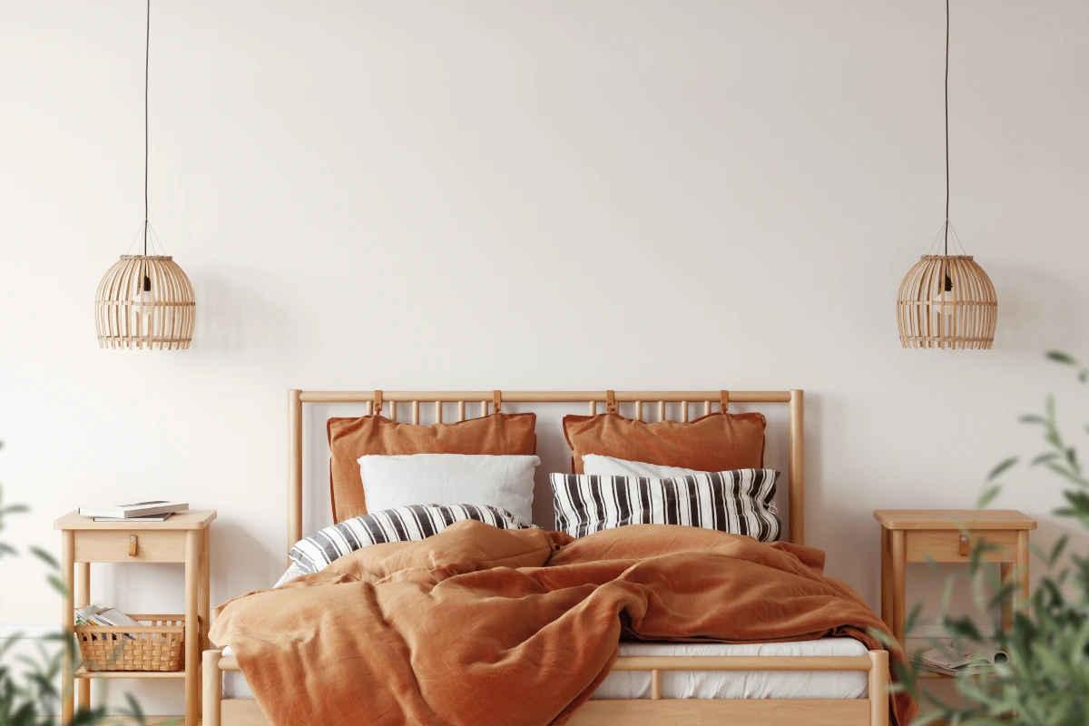 Konstrukcja łózka wraz z materacem oraz poduszkami oraz narzutami w kolorze ceglanym. Obok łóżka stoją dekoracje w stylu boho.