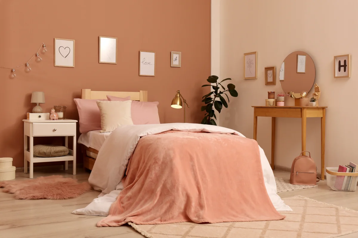 Łóżko o drewniane konstrukcji z pościelą oraz poduszkami w kolorze różu. Na ścianie obrazy.