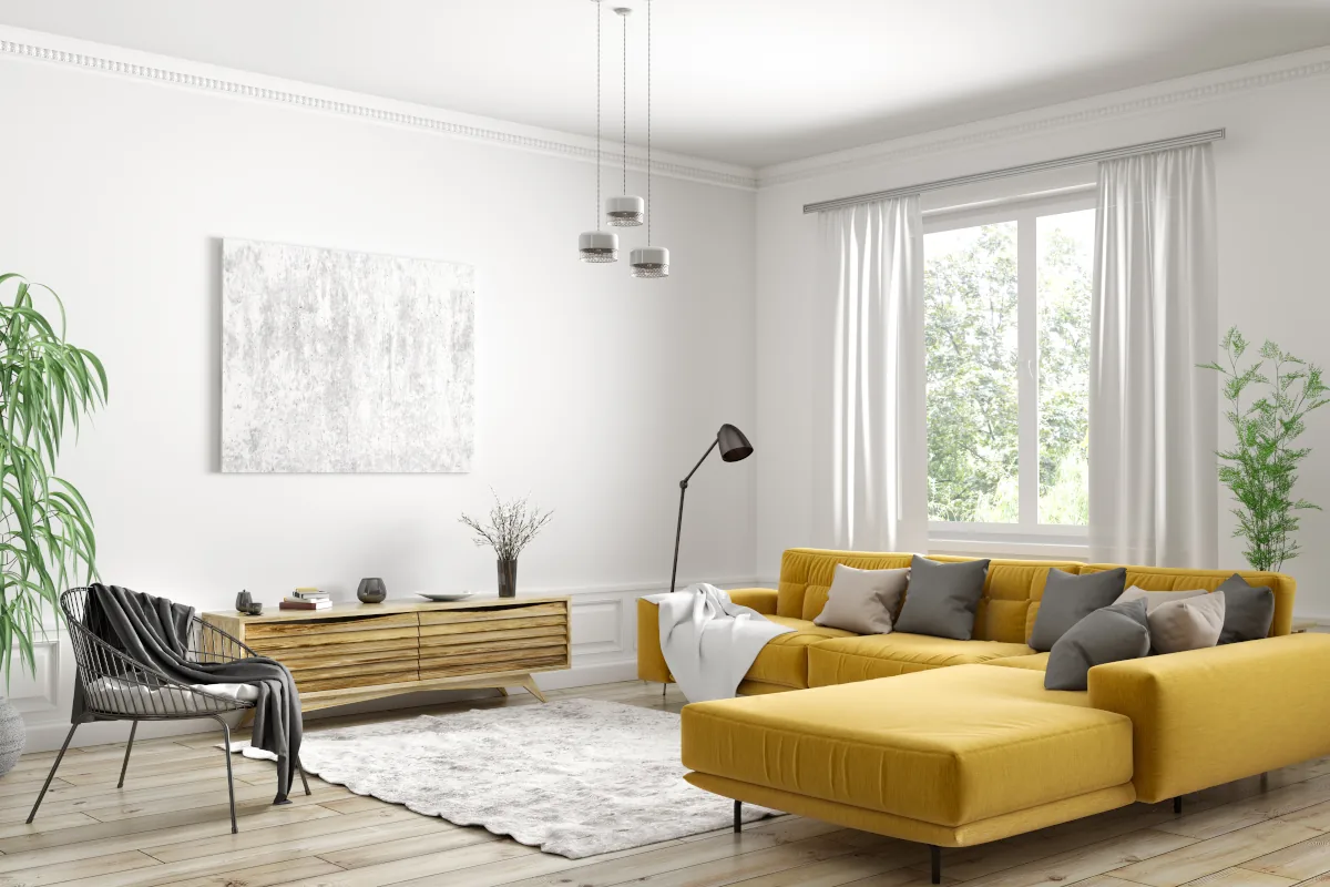 Duża, żółta, narożna kanapa w salonie w odcieniu bieli. Obok fotel oraz szafka pod ścianą.