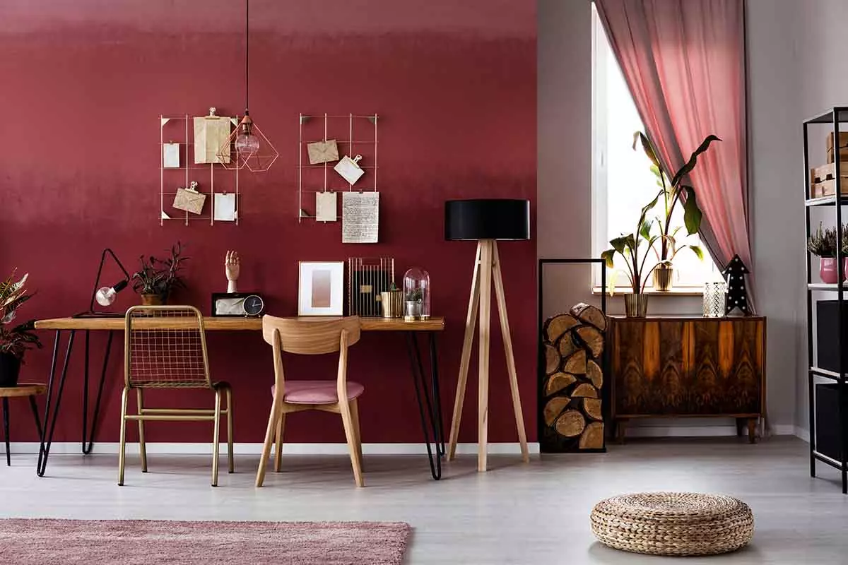 Kolor Viva Magenta na ścianie. Przy ścianie stolik z dekoracjami.. Krzesła drewniane oraz lampa stojąca obok stolika. Zasłony również w podobnych kolorach co ściana.