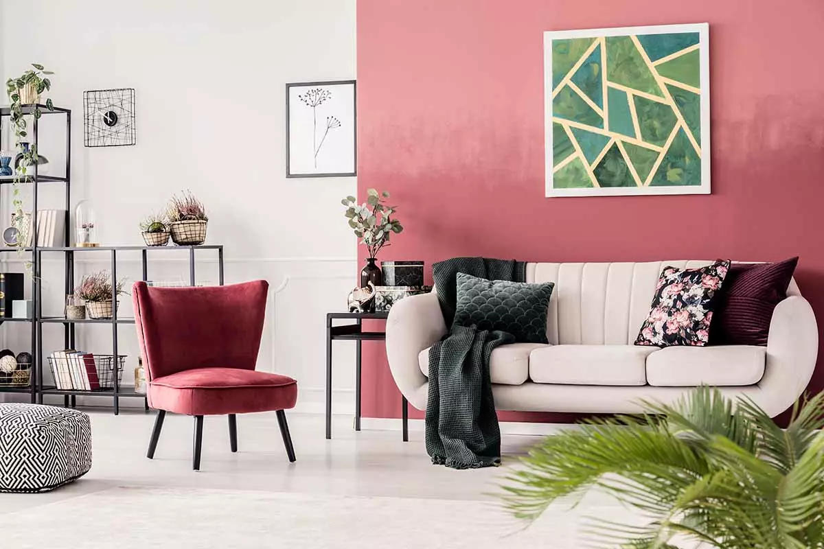 Viva magneta na ścianie. Pod ścianą stoi kanapa z poduszkami oraz kwiatami. Obok różowy fotel, a tle regały z dekoracjami.