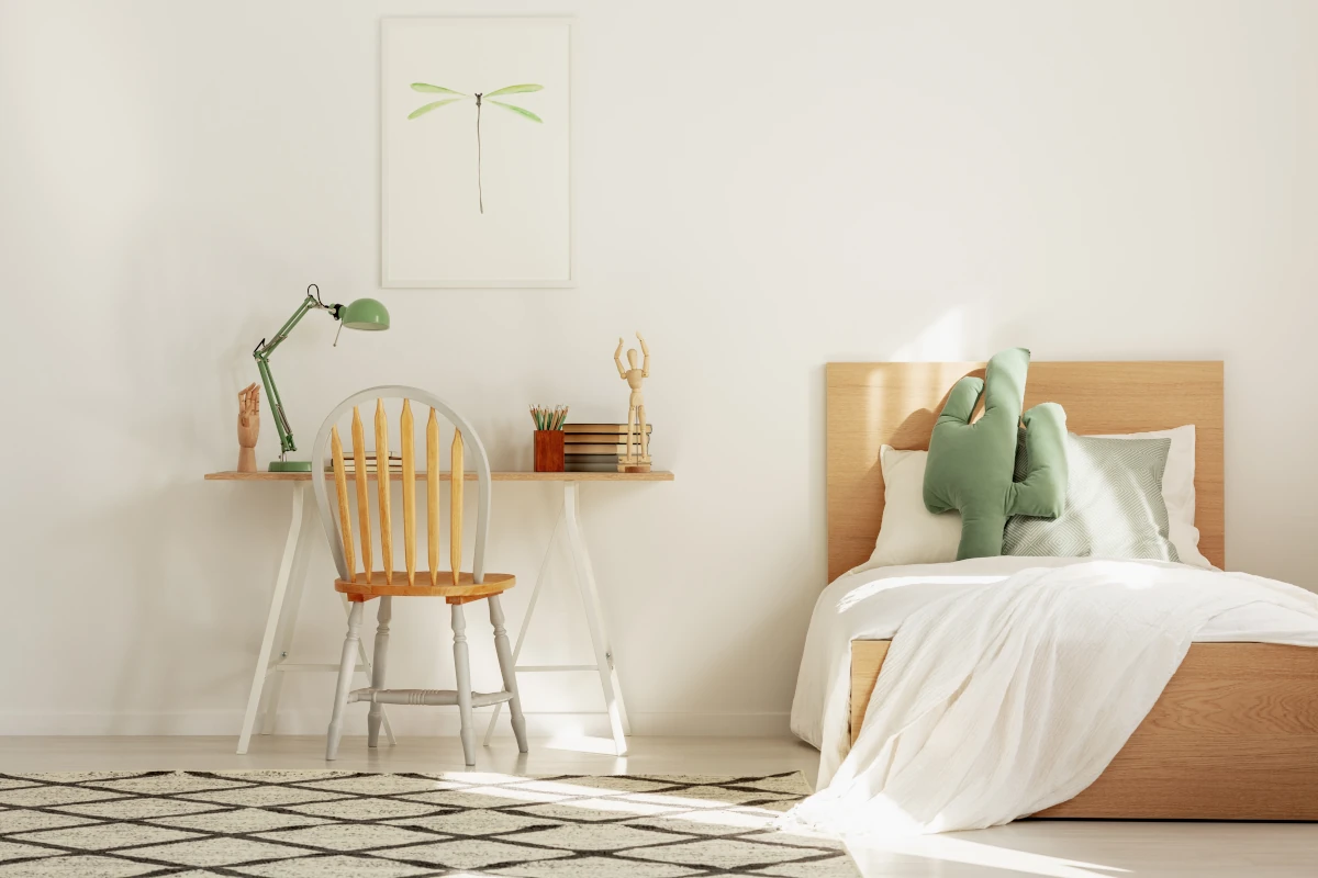 Łóżko w pokoju dziecka w stylu skandynawskim. Obok łóżka postawione biurko z lampką, figurką oraz książkami na blacie.