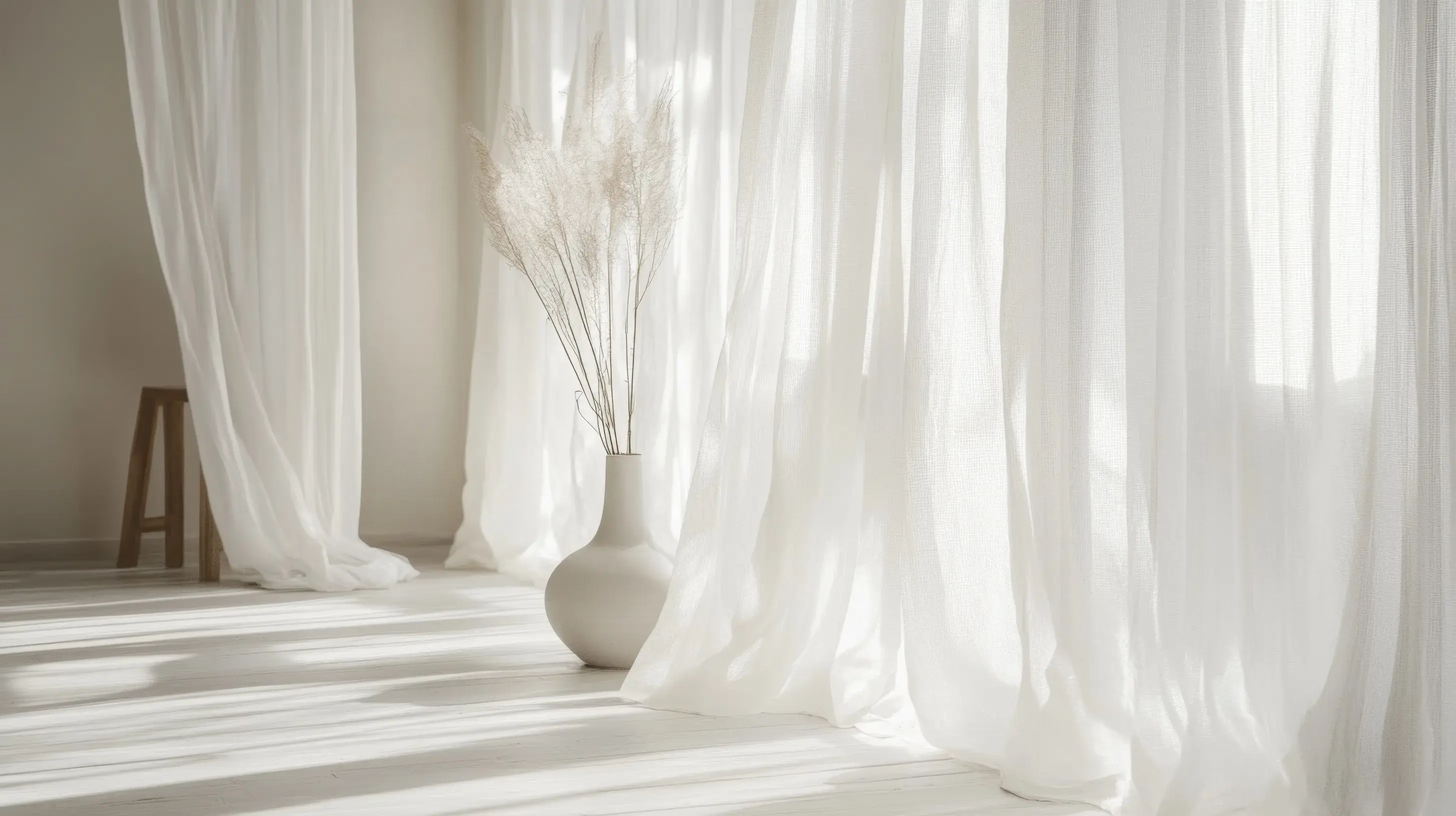 Salon w stylu japadni w odcieniach koloru Pantone 2026 Cloud Dancer z wielkimi oknami, przed którymi wewnątrz wiszą firanki i dużym wazonem, w którym są kwiaty. 